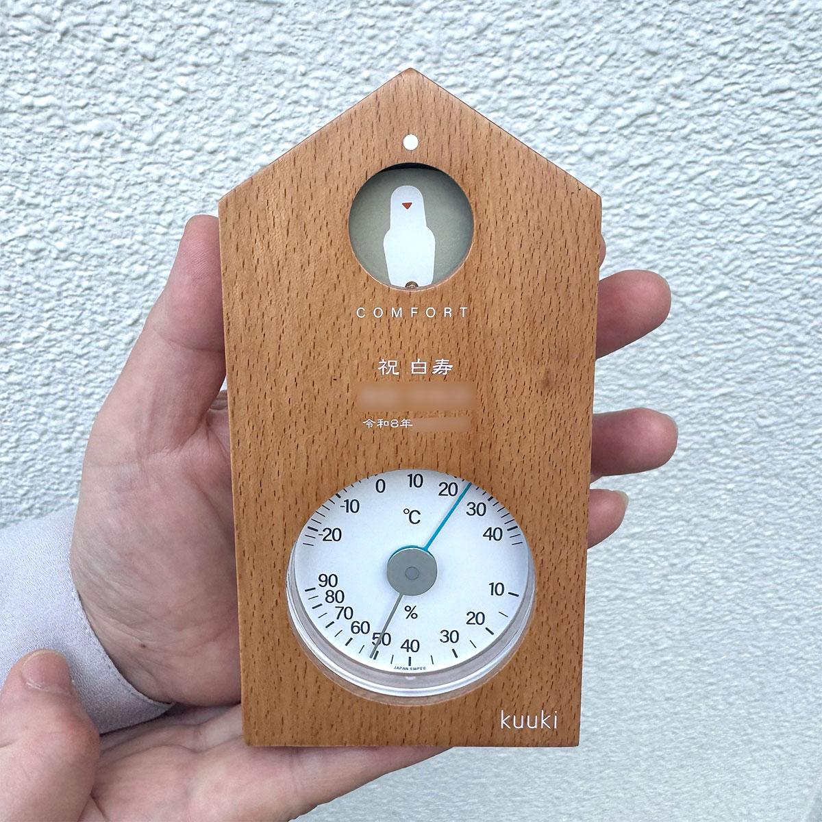 ハト温湿度計ナチュラルの白寿祝い用名入れオーダー実例。「祝 白寿」の文字と日付、贈り主様の温かいお祝いメッセージが木目に刻印された世界にひとつのギフト